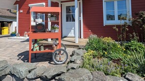 Ein rotes Haus mit Veranda, Steinmauer und Pflanzwagen.