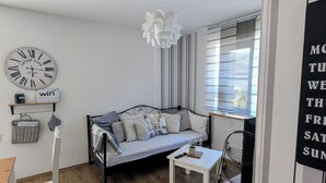 Ein modernes Wohnzimmer mit einer Couch, einem kleinen Tisch, einem Sessel, einer Pendelleuchte, einer Vintage-Uhr und einem Schild mit teilweise lesbarem Text.