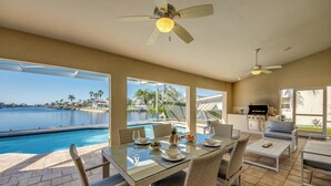 Un vaste espace extérieur aménagé pour les repas, avec une table en verre, des chaises en osier et une vue sur une piscine et l’océan.