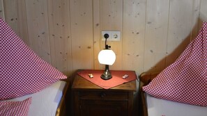 A wooden-paneled room with a nightstand, a lamp, and checkered pillows. - Double / Breakfast With View to Sorgschrofen - Landhaus Windrose (Jungholz)