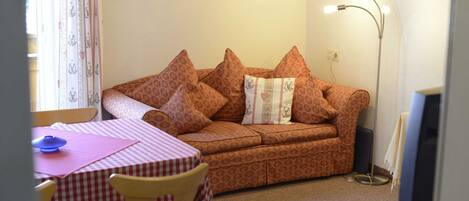 A living room with a sofa, a table with a checkered tablecloth, a lamp, and a framed picture on the wall.
