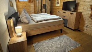Ein Schlafzimmer einer Holzhütte mit Bett, Nachttisch, Lampe, Fernseher und einem gemusterten Teppich.