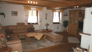 Ein gemütliches Wohnzimmer mit einer Couch, einem Sessel und einem Couchtisch. Es gibt ein Schrank mit Glastüren und einen Fernseher.