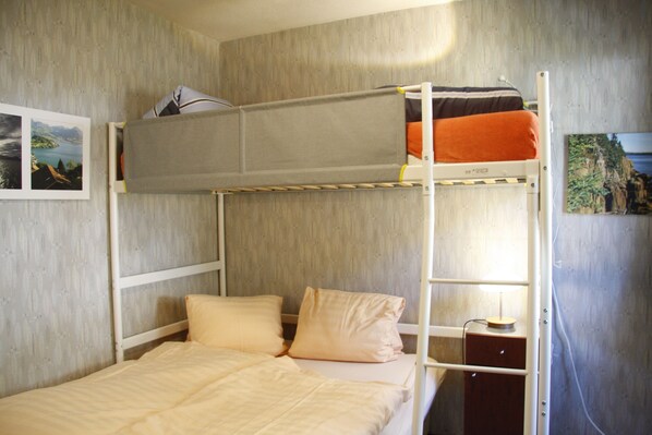 A bunk bed room with a wooden headboard, a nightstand with a lamp, and a painting on the wall.
