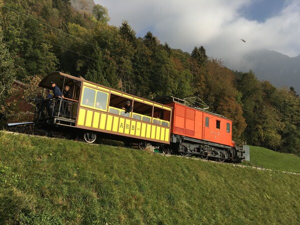 Un wagon de train ancien aux couleurs jaune et rouge, situé sur une voie ferrée avec une chaîne de montagnes en arrière-plan.