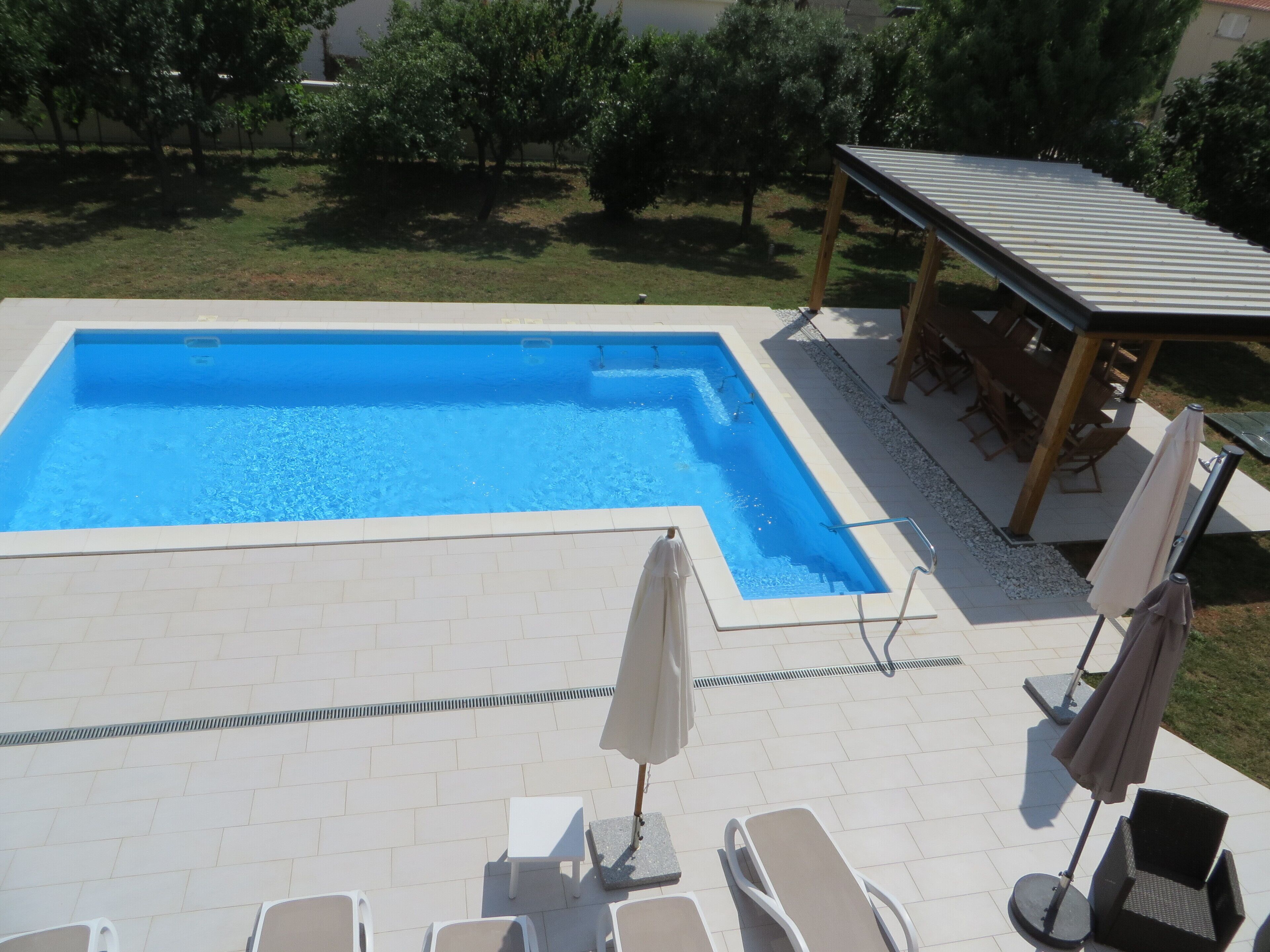 Ein rechteckiger Pool mit gefliestem Sonnendeck, umgeben von Liegestühlen und Sonnenschirmen.