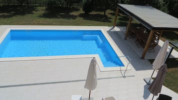 Une piscine rectangulaire avec une terrasse carrelée, entourée de chaises longues et de parasols.
