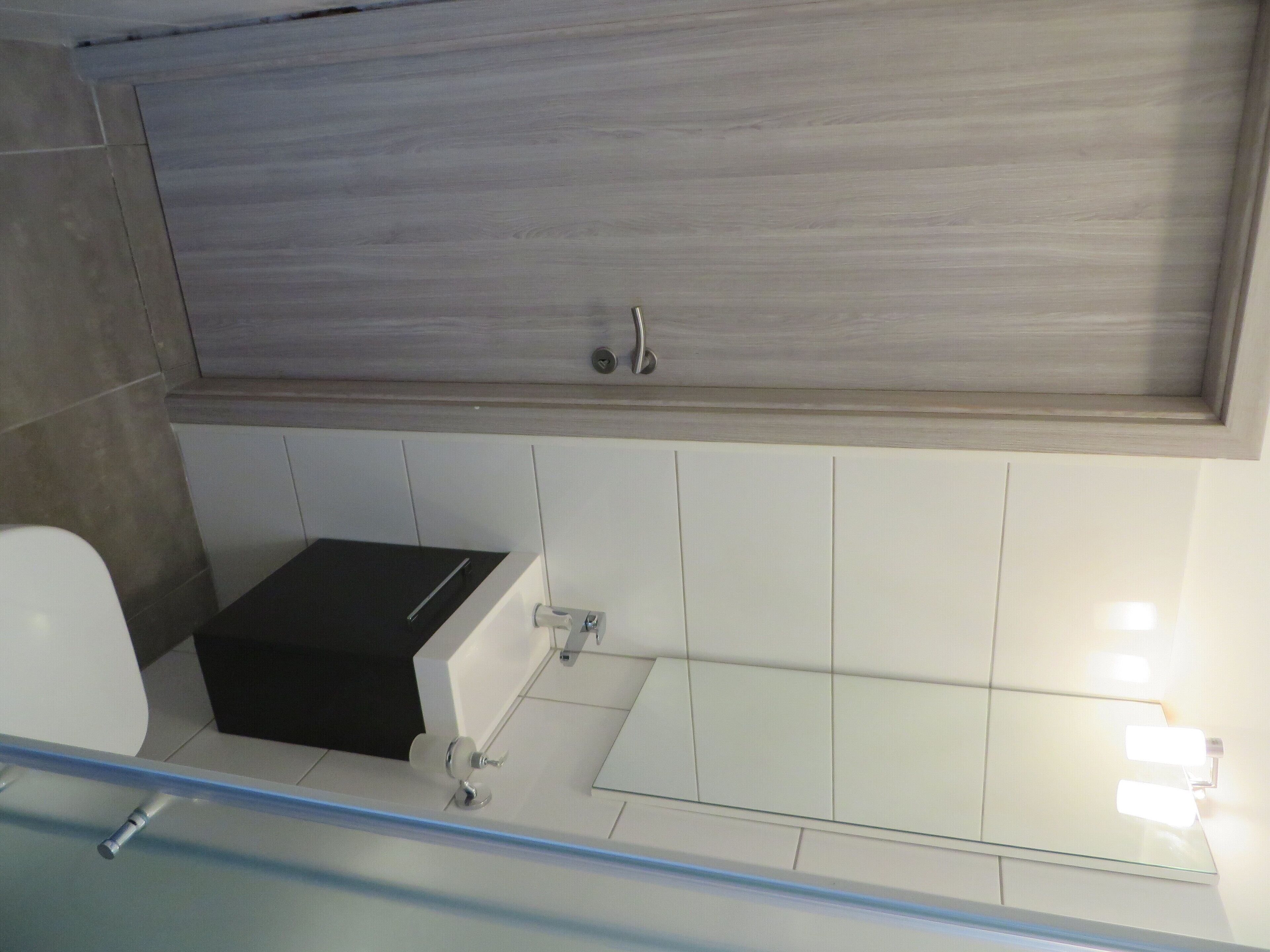 Ein modernes Badezimmer mit einem Holz-Waschtisch, einem schwarzen Waschbecken und einer Duschkabine aus Glas.