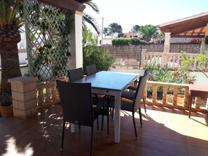 Une terrasse extérieure avec une table et des chaises, entourée de plantes et d’une clôture.