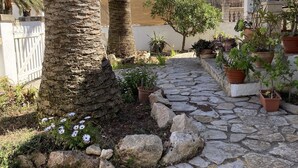 Een patio met stenen bestrating, palmbomen, potplanten en een witte poort.