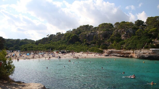 Een strand met helder turquoise water, een zandstrand en rotsachtige kliffen.