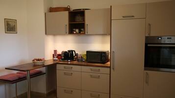 Eine kompakte Küche mit Mikrowelle, Toaster und Kaffeemaschine auf der Arbeitsplatte, einem kleinen Kühlschrank und einem Schrank mit Korb oben.