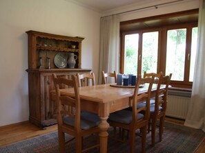 A dining room with a wooden table and chairs, a cabinet with dishes, and a window with curtains. - Holiday house Enke, Germany (Miesbach)