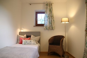 A bedroom with a bed, a chair, a floor lamp, a window with curtains, and a small window above the bed. - Holiday house Enke, Germany (Miesbach)