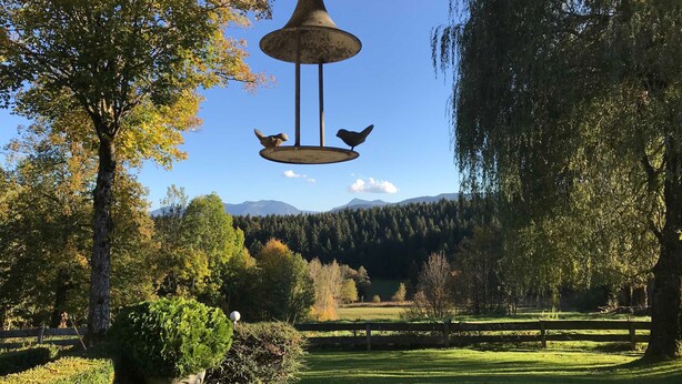 Un parque con una campana colgante, árboles, una valla de madera y una cadena montañosa distante.