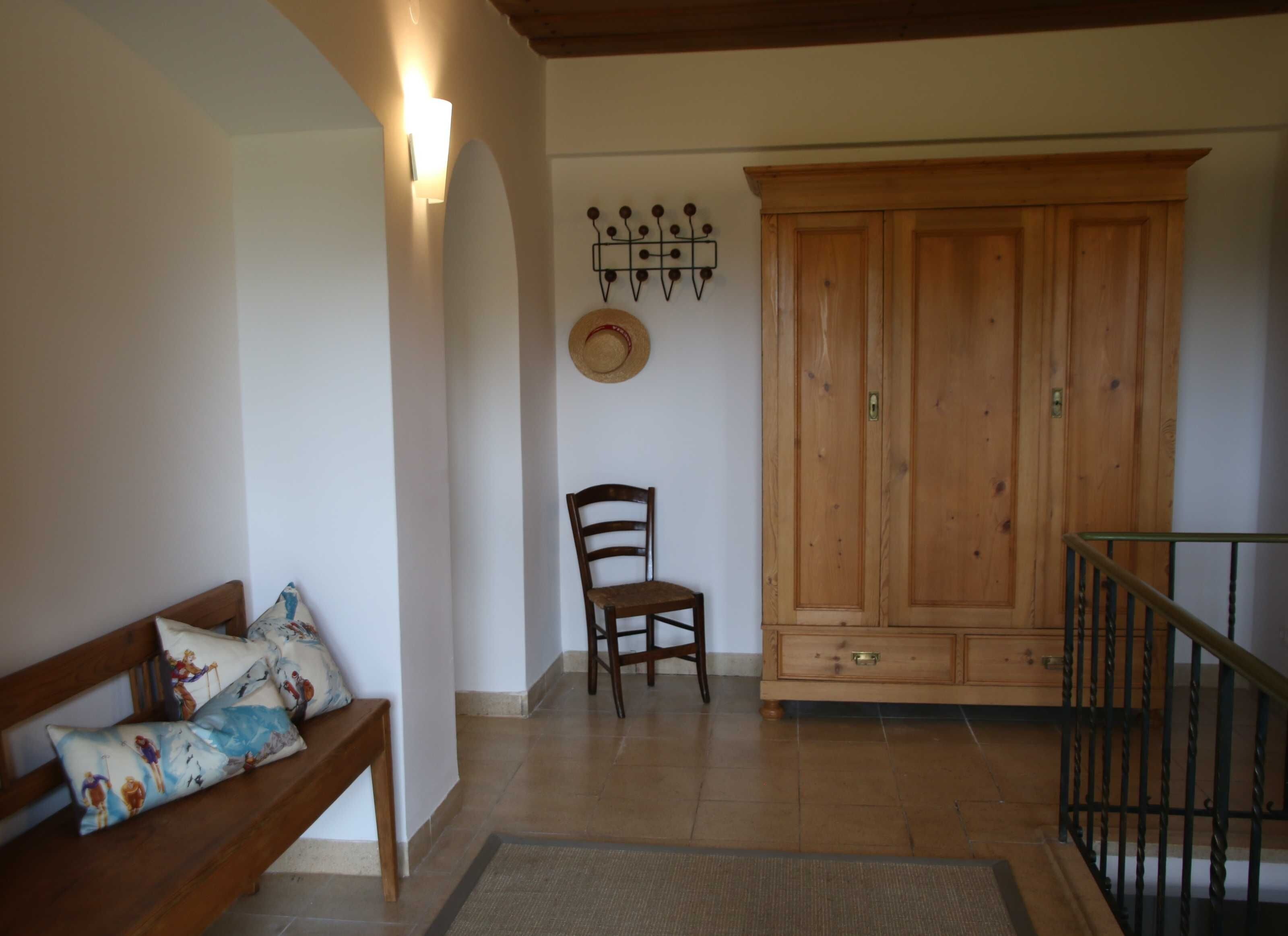 A room with a wooden bench, a chair, a wardrobe, and a wall-mounted light fixture.