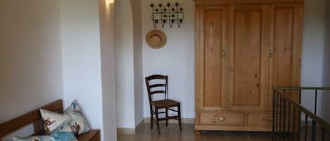 A room with a wooden bench, a chair, a wardrobe, and a wall-mounted light fixture.