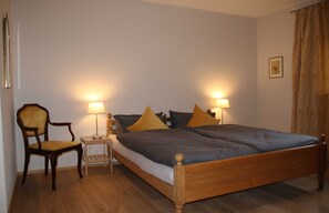 A bedroom with a wooden bed, two bedside tables with lamps, a wooden chair, and a small bedside table with a lamp. - Holiday house Enke, Germany (Miesbach)