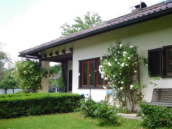 A house with a covered porch, a window with shutters, and a garden with various plants. - Holiday house Enke, Germany (Miesbach)