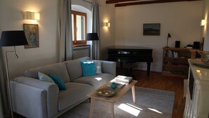 Una sala de estar con un sofá, un piano, una mesa de centro y una estantería.