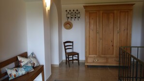 Una habitación con un banco de madera, una silla, un armario y una lámpara fijada a la pared.