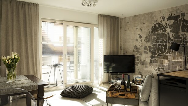 A modern living room with a flat-screen TV, a dining table with chairs, a sofa, and a window with curtains. - FEWO-KARLOTTA New 2-room / 5 min. Ammersee & Zentrum- LUXURY in the heart of Dieessen! (Diessen)