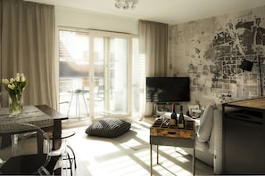 A modern living room with a flat-screen TV, a dining table with chairs, a sofa, and a window with curtains. - FEWO-KARLOTTA New 2-room / 5 min. Ammersee & Zentrum- LUXURY in the heart of Dieessen! (Diessen)