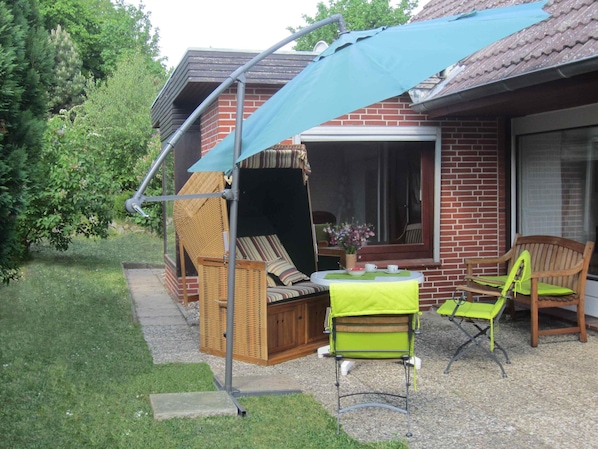 A patio with a covered seating area, a table with a bowl and cups, and a window overlooking the garden. - 4 - **** apartment, large garden and terrace with beach chair; quiet surroundings (Heiligenhafen)