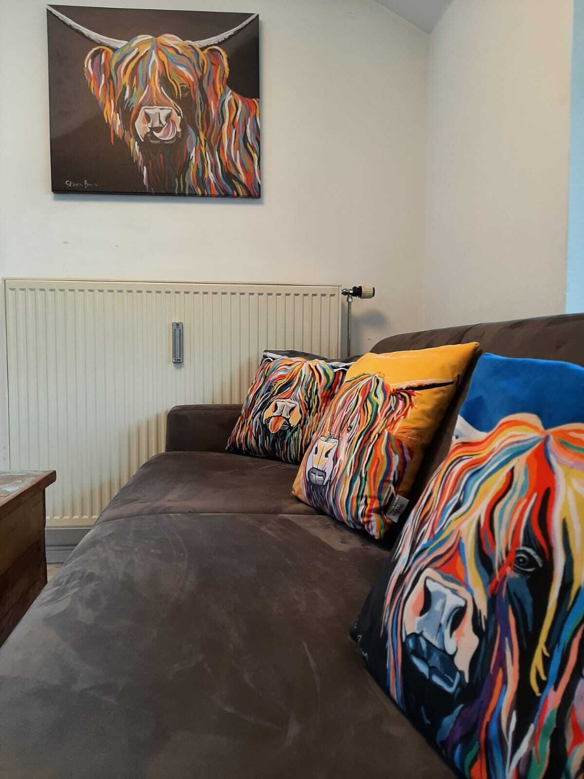 A bedroom with a brown sofa bed, colorful pillows, a white radiator, and a painting of a dog on the wall.
