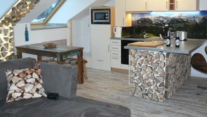 Uma cozinha moderna com ilha de pedra, área de refeições com mesa de madeira e um espaço de estar aconchegante com almofada estampada.