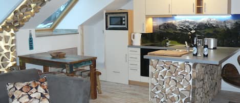 A modern kitchen with a stone island, a dining area with a wooden table, and a cozy seating area with a patterned cushion.