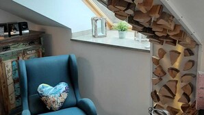Uma sala de estar moderna com uma poltrona azul, um painel de parede de madeira e uma pequena janela com uma planta.