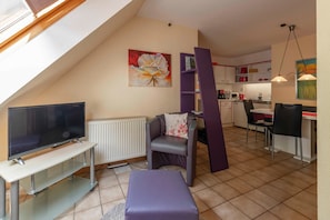 A modern living room with a TV, seating, and a kitchen in the background. - Vacation apartment 3 - House Wiesenttal (Waischenfeld)