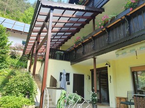A two-story building with a wooden balcony, a covered patio, and a garden area with potted plants. - Vacation apartment 3 - House Wiesenttal (Waischenfeld)