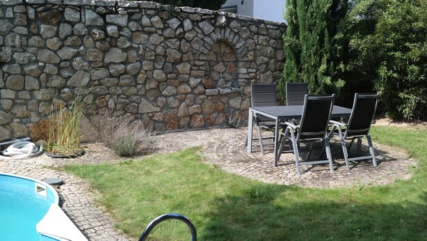 Eine Steinsäule, ein Pool und eine Terrasse mit Tisch und Stühlen.