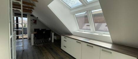 A modern kitchen with a skylight, wooden flooring, and white cabinetry.