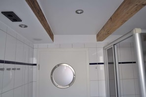 Een moderne badkamer met witte tegels, een ronde spiegel, houten balken en een douchecabine van glas.