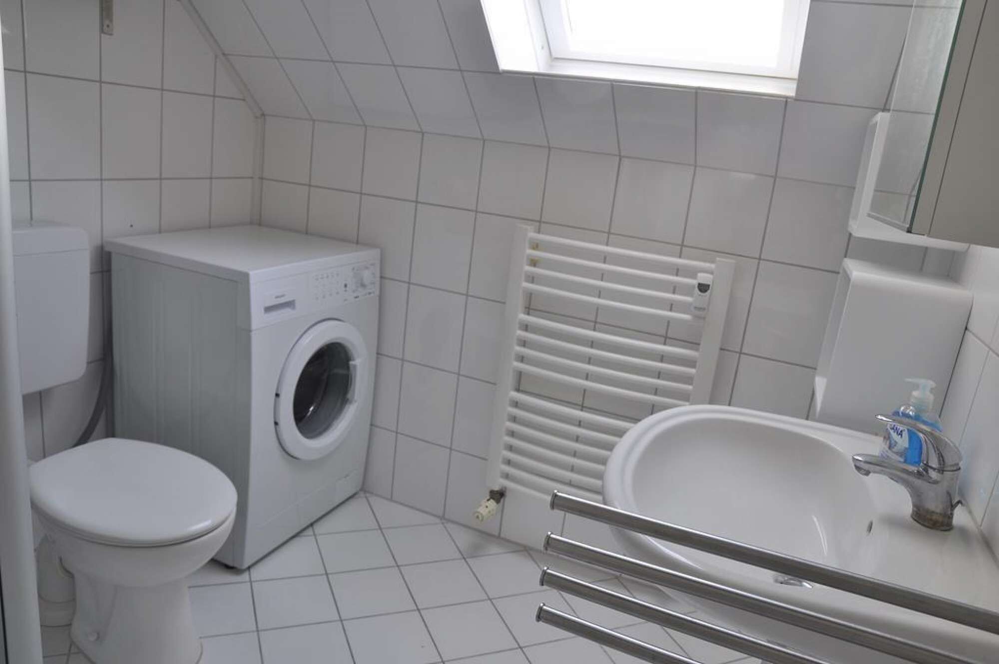 A small, modern bathroom with a washing machine, toilet, and sink.