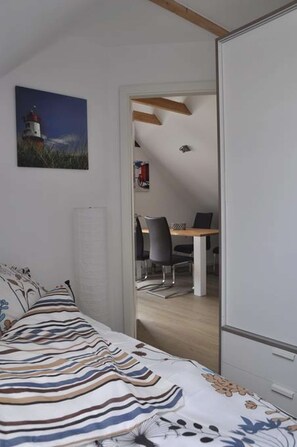 A bedroom with a bed, a desk, and a chair in the adjacent room.