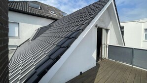 Un edifici residencial amb teulada inclinada, una finestra visible i un balcó de fusta.