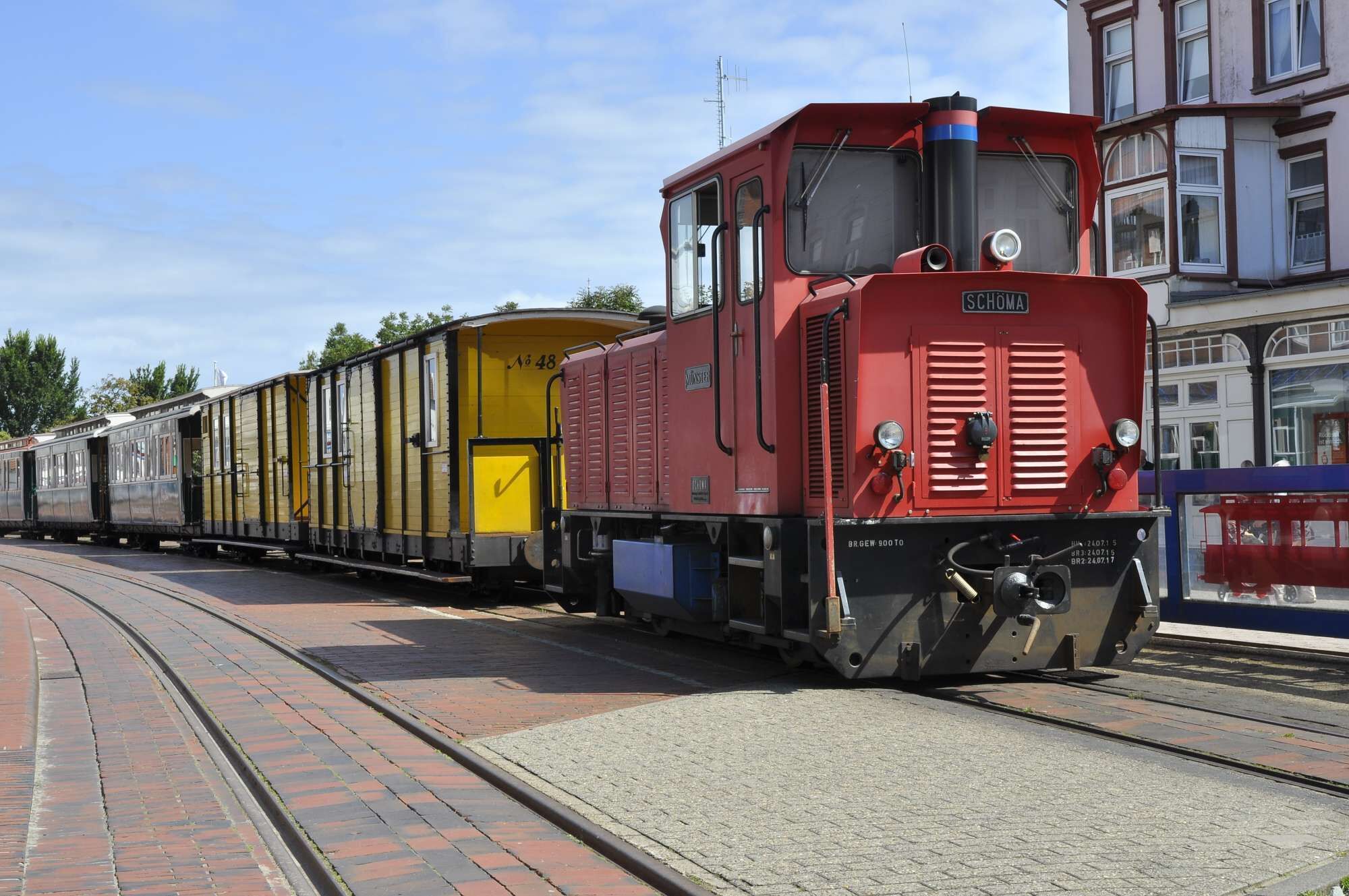 A red train with yellow and grey carriages on a brick-paved track.