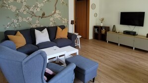 A living room with a sofa, armchairs, a coffee table, a TV, and a bookshelf. - Beautiful vacation apartment with large outdoor terrace near the dike (Simonsberg)