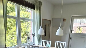 A dining area with a table and chairs, a window with curtains, a radiator, and a door. - Beautiful vacation apartment with large outdoor terrace near the dike (Simonsberg)