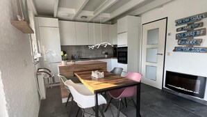 A modern kitchen with white cabinets, a wooden island, and a dining area with a table and chairs. - Detached holiday home in a quiet location, right on the Grevelingenmeer (Herkingen)