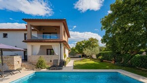 A two-story house with a swimming pool, a covered patio, and a well-maintained garden.