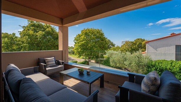 A covered outdoor seating area with a table, chairs, and a view of greenery and a building.