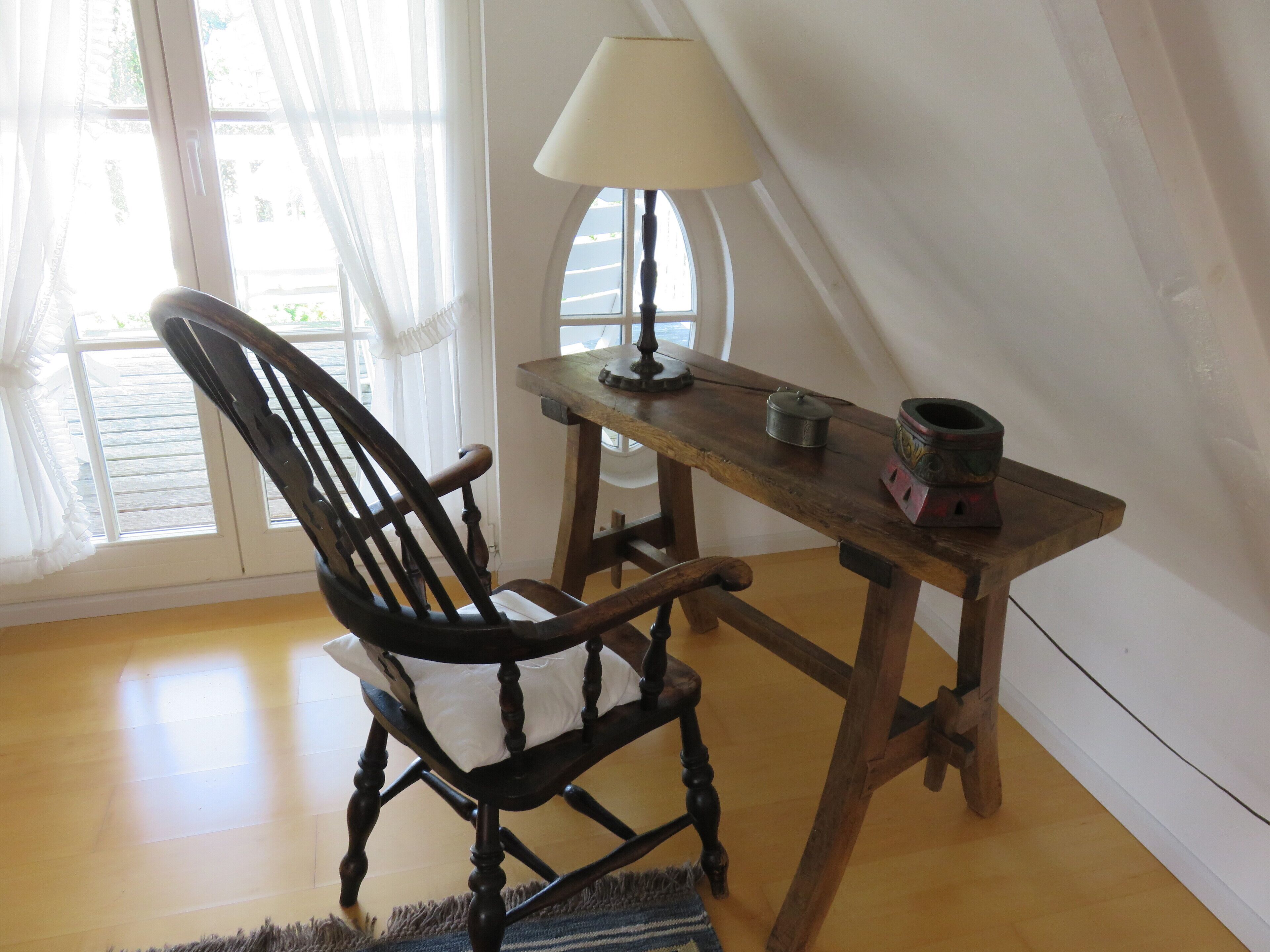 A wooden chair and table in a room with a window and a lamp.