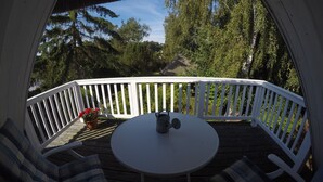 A deck with a round table and two chairs, surrounded by a white railing, overlooking a forested area. - Landhaus Darss - in love with nature (Wieck a. Darß)