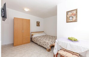 Une chambre à coucher avec un lit, une armoire, une petite table sur laquelle se trouve un vase, et un tableau accroché au mur.