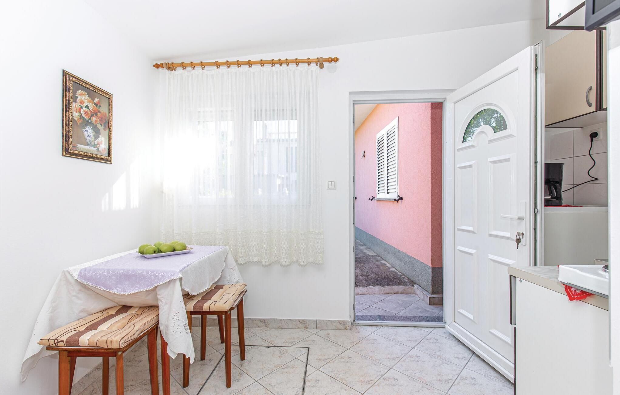 A small kitchen with a table and chairs, a white door, and a view of a pink building outside.